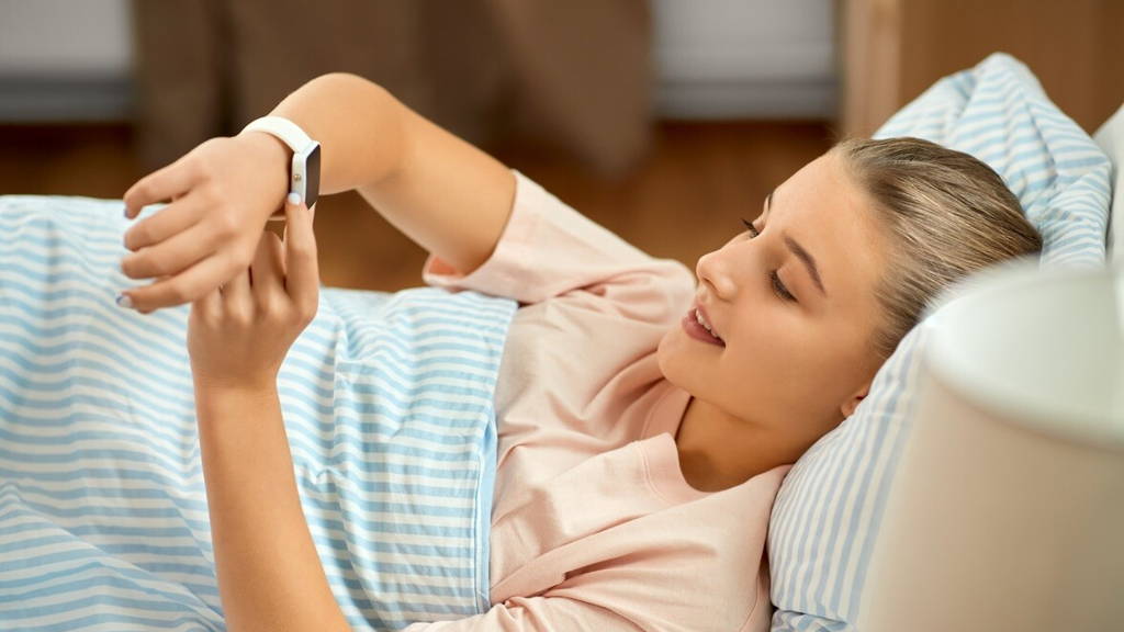 smiling girl with smart watch lying in bed at home