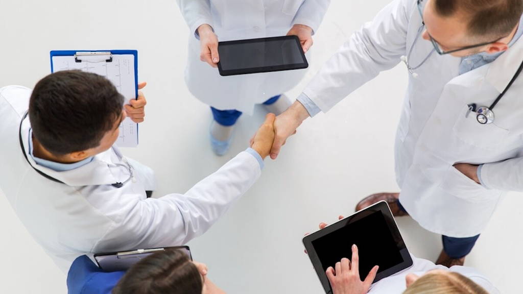 doctors with tablet pc doing handshake at hospital