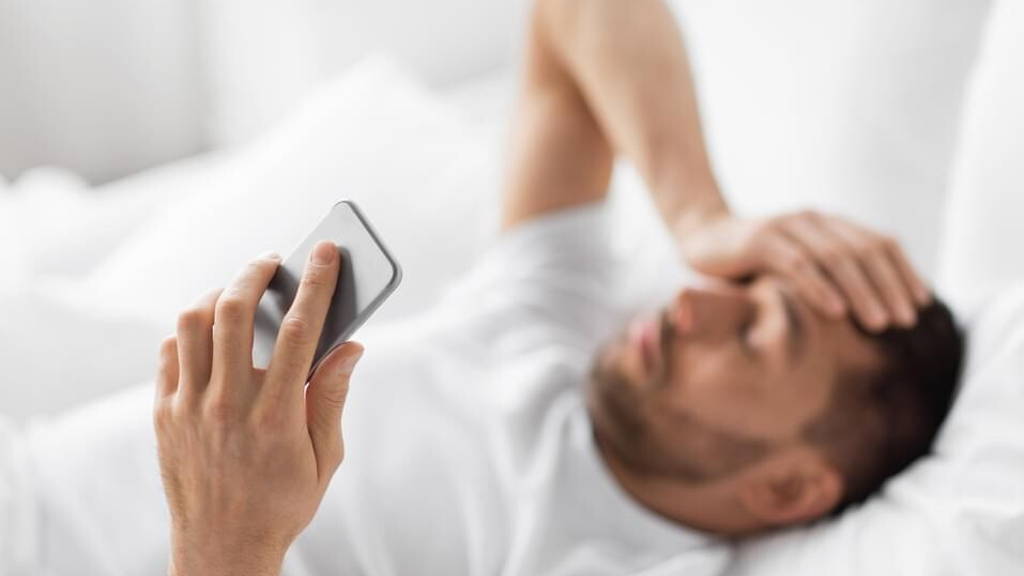 hand of young man with smartphone in bed