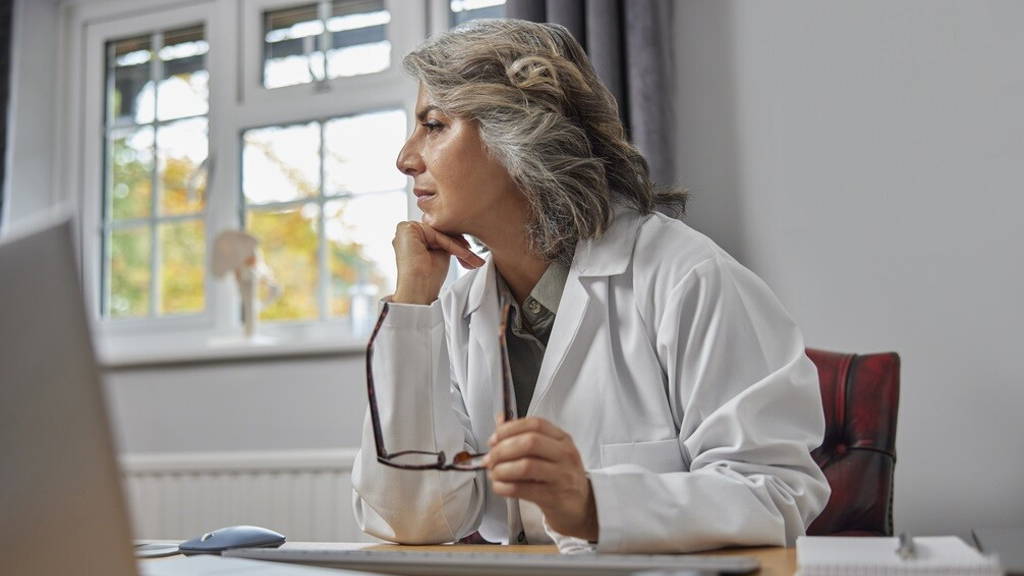 Stressed And Overworked Mature Female Doctor Wearing White Coat