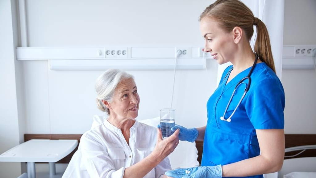 nurse giving medicine to senior woman at hospital