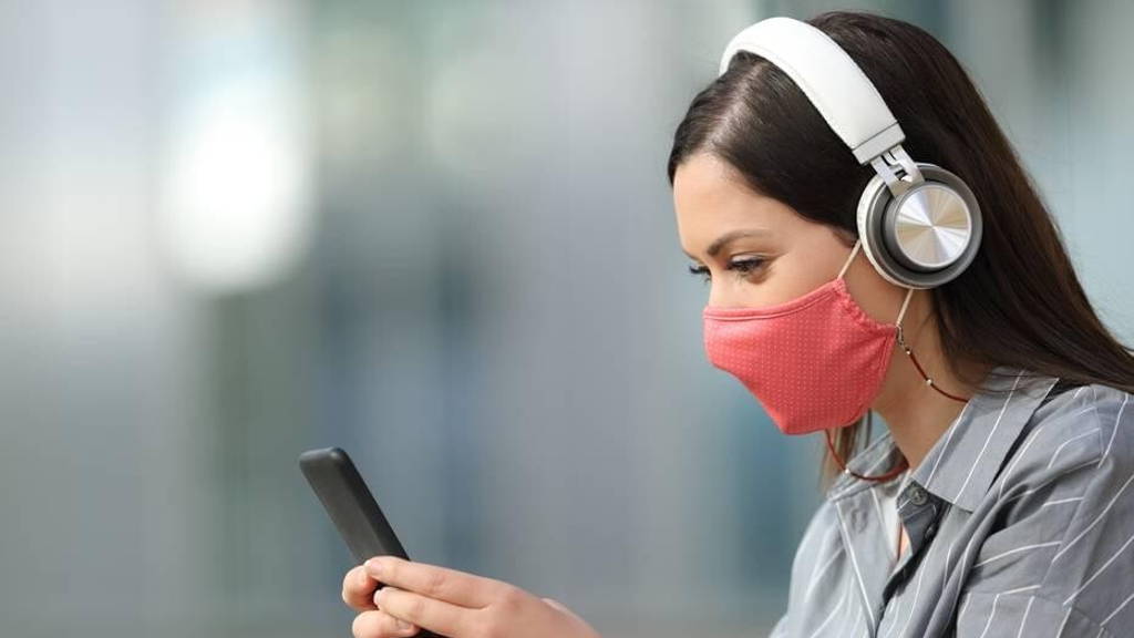 Woman with mask listening to music from smart phone