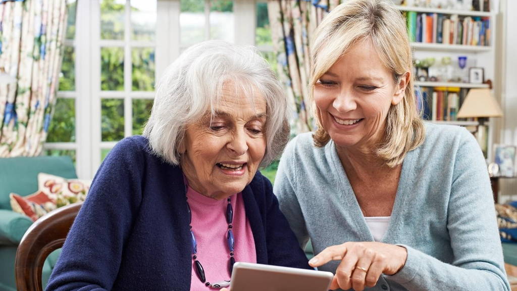 Female Neighbor Showing Senior Woman How To Use Digital Tablet