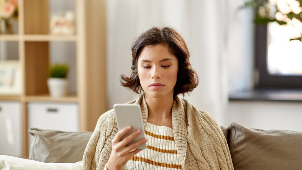 sad woman in blanket using smartphone at home